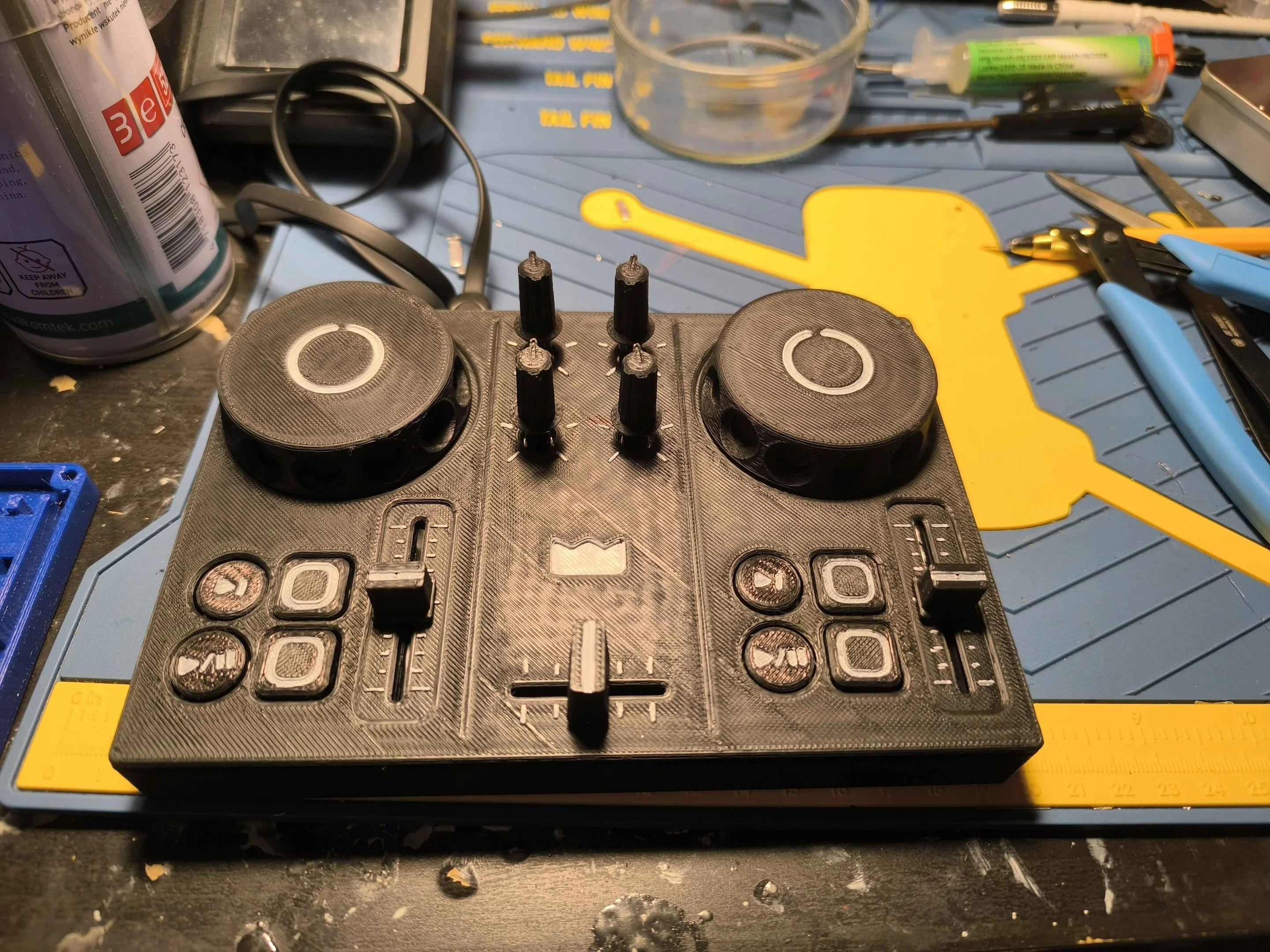 DJC-DIY, a DIY DJ controller, printed in black and standing on a workbench beside pliers, a syringe of flux and a cutting mat